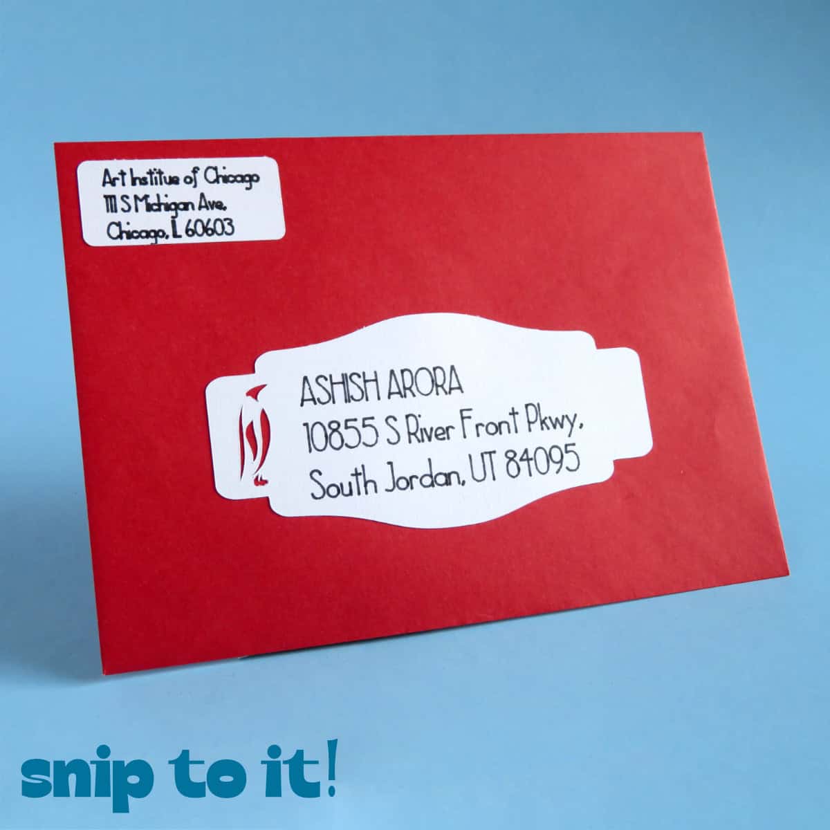red envelope with a white address label and a penguin cut out embellishment, set against a blue background.