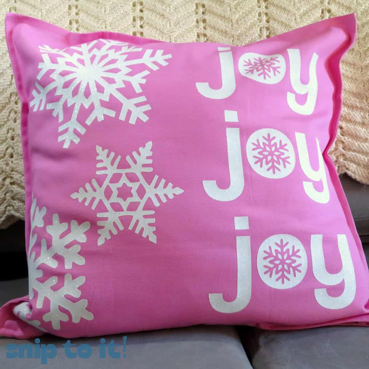 bright pink throw pillow decorated with a large white glitter snowflake design and the words JOY JOY JOY