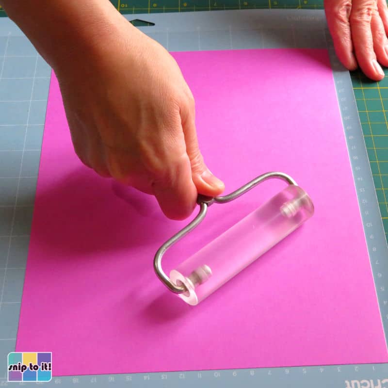 photo of attaching the pink/base layer of cardstock to the cutting mat using a brayer