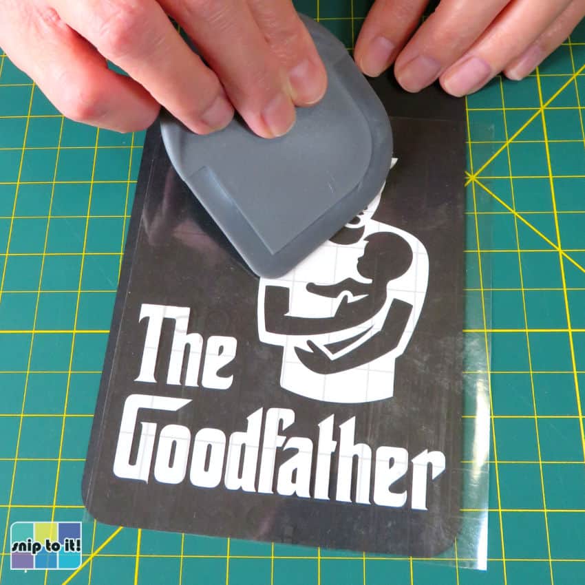 closeup image of adhesive vinyl on transfer tape being lightly burnished onto cardstock panel