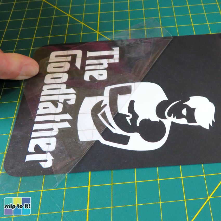 closeup image of transfer tape being peeled off adhesive vinyl that has been applied to a piece of black cardstock