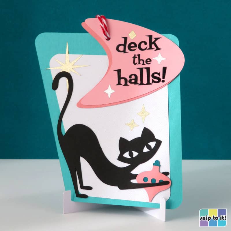 gift card holder ornament in mid century style, made using pink and turquoise cardstock and with an atomic cat playing with a vintage ornament and "deck the halls" on a boomerang shape