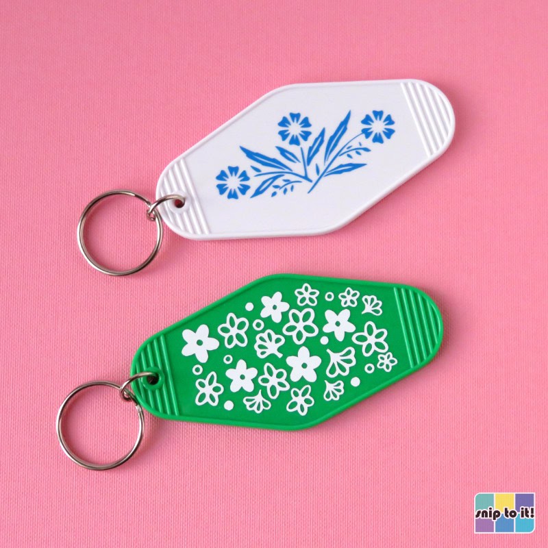 green motel keychain decorated with white vinyl in pyrex spring blossom pattern, shown with white motel keychain decorated with blue vinyl in corningware cornflower pattern