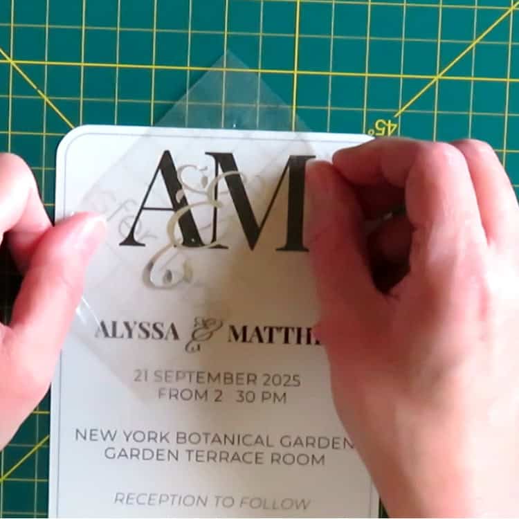 closeup image of Cricut adhesive foil vinyl being applied as the second layer of an intertwined wedding monogram on a custom invitation