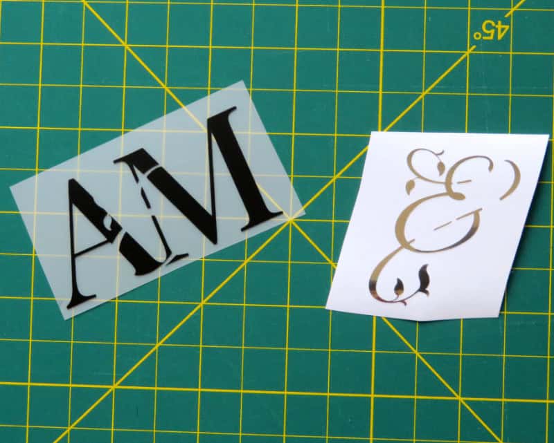 closeup image of two layers of the monogram cut out of black matte vinyl and silver adhesive foil. The image reveals that the two layers will fit together like jigsaw puzzle pieces and create a single cohesive monogram that will appear to be a delicate, luxurious script ampersand intertwining a pair of bold, formal serif initials