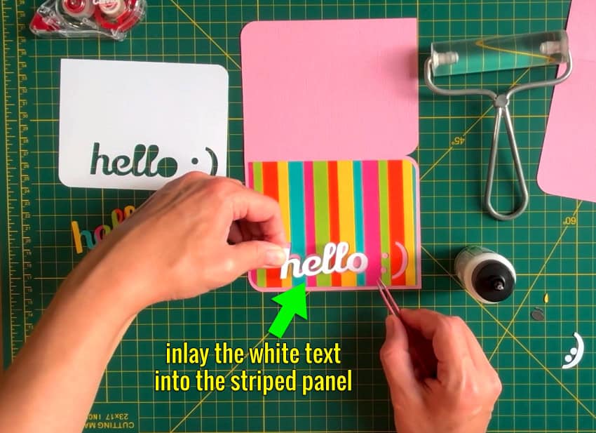 photo showing assembly of an inlay card. White cardstock text is being inlaid into the striped front panel of the card, which is already adhered to the card base