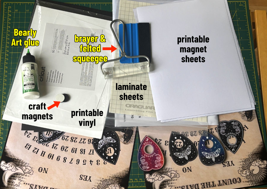 photo of materials required to make the ouija inspired halloween countdown calendar: printable magnet sheets, laminate/overlay sheets, felted squeegee, brayer; for making the 3D planchette magnets: heavy cardstock, printable vinyl, glue, and self-adhesive craft magnets