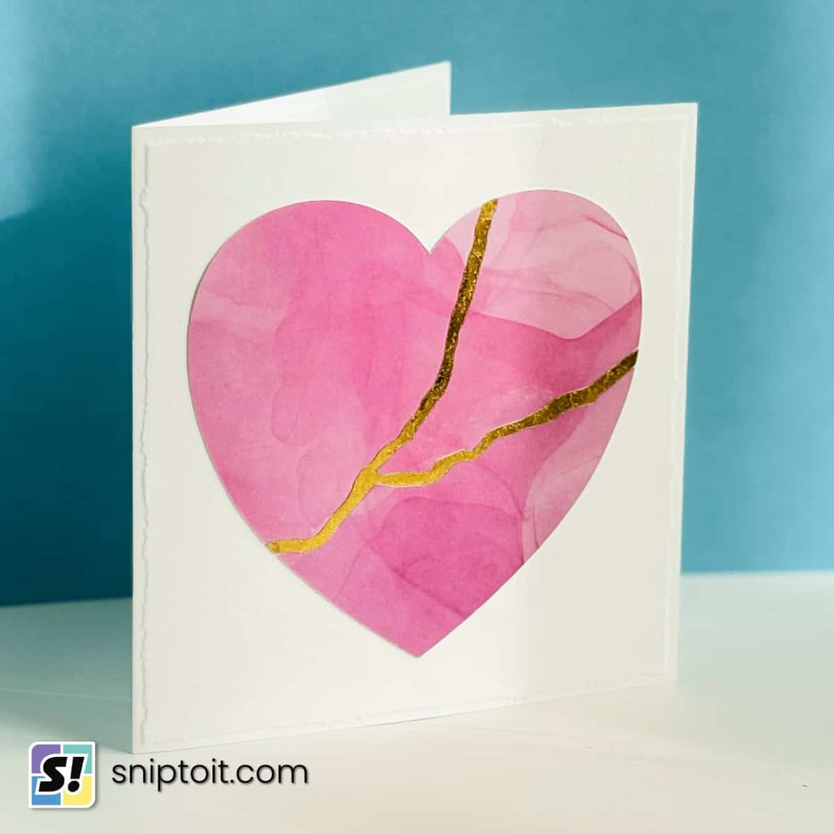 white greeting card with a faux-deckle edge, featuring a pink cardstock heart decoration stylished to look like it has been broken and mended in the kintsugi style. The effect is achieved using Cricut gold foil and adhesive cardstock