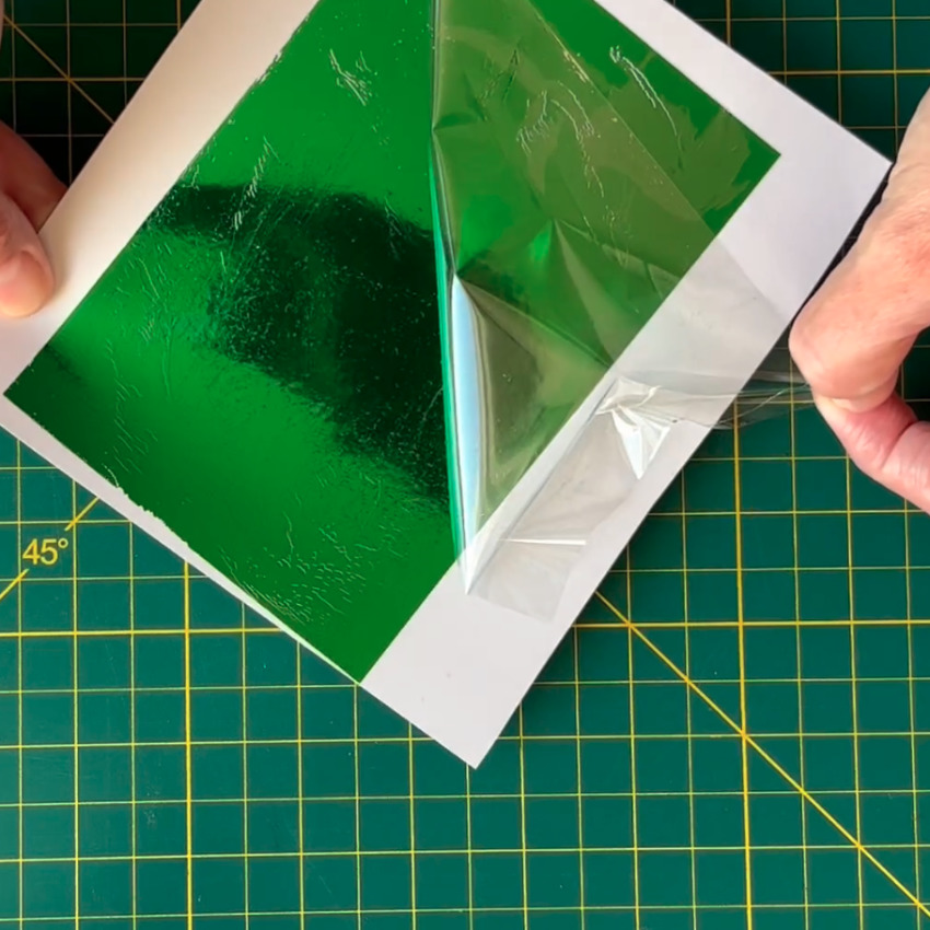 photo showing composition of Cricut foil sheet - a plastic carrier and a foil layer. Photo shows foil layer applied to an adhesive sheet
