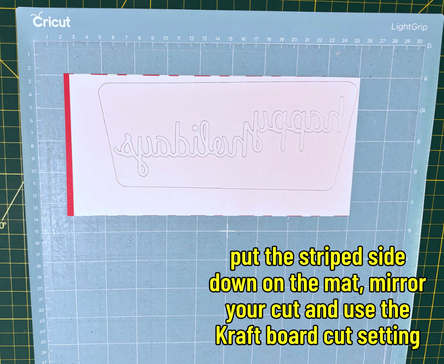 image of the striped cardstock facedown on a cricut lightgrip mat, with a midcentury rhombus shape and the words Happy Holidays cut in reverse