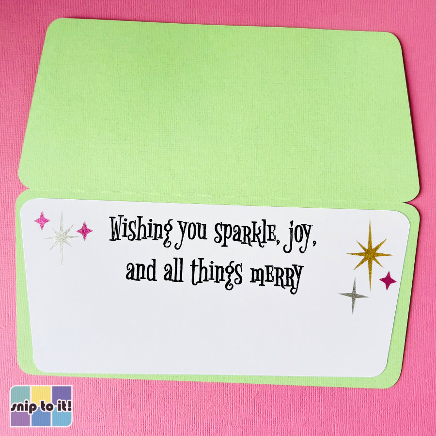 image of the inside of the finished pink and green mid-century Christmas card. It features a white panel mounted on green cardstock with the written sentiment "Wishing you sparkle, joy, and all things merry" in a whimsical 1950s serif font. The inside of the card is embellished with gold, silver and ink shimmer vinyl stars