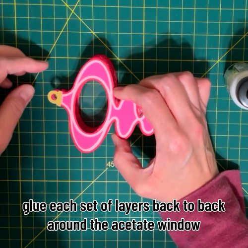 the two sides of the ornament are being glued together back to back with the acetate window sandwiched between them