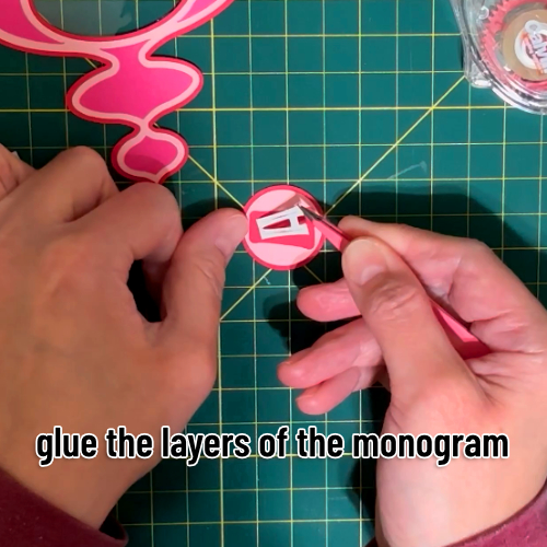 the cardstock layers of the monogram are glued together: two red and pink circles on top of each other, then a capital letter A in the font Crava is laid on top of a red offset layer
