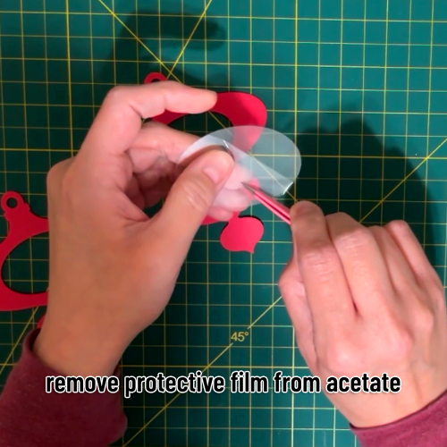 protective film on a piece of acetate being removed with a pair of tweezers before being glued to the back of the cardstock layers