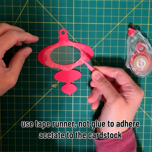 acetate window being laid in place onto a stripe of pressure sensitive adhesive on the back of the base layers of the cardstock ornament
