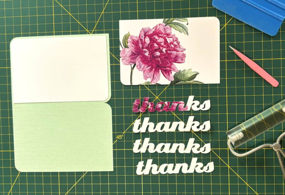photo showing all the pieces of the eclipse card cut out and ready for assembly. Card base is green pastel 80lb cardstock, inside panel is white 65lb matte cardstock. 3 copies of "thanks" spacer text are 80lb white cardstock. Base panel and top printed text are both printed on glossy 80lb white cardstock. Also seen are tweezers and brayer for assembly.